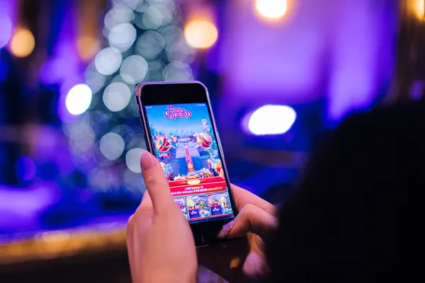 A young woman relaxing with her phone while dynamic casino elements float around her, illustrating the smooth mobile experience offered by the 456BD app.